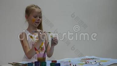 可爱的小女孩画家在桌子上画画，在她的衣服上画画。 慢动作