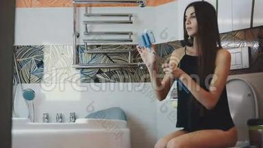 有魅力的女孩坐在浴室里的厕所里，带着蓝色的monopod自拍