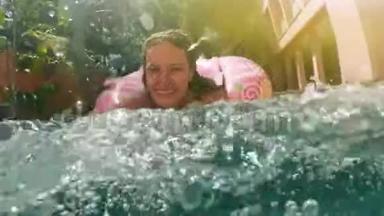 阳光明媚的<strong>夏日</strong>，戴着蓝色比基尼太阳镜的女人躺在充气的粉红色甜甜圈里漂浮在<strong>游泳</strong>池里。 看镜头
