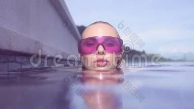 在阳光明媚的一天，年轻女子戴着紫色太阳镜在无限屋顶游泳池里看相机。