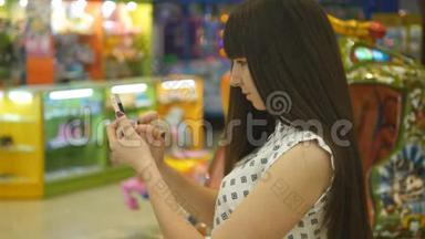 年轻女子在购物中心玩室内游戏，使用智能手机。 女孩玩流行的智能手机游戏-捕捉
