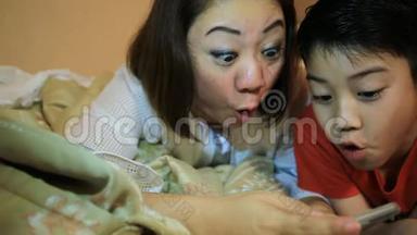 快乐的亚洲家庭在床上玩智能手机时玩得开心，在卧室里