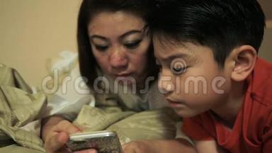 快乐的亚洲家庭在床上玩智能手机时玩得开心，在卧室里