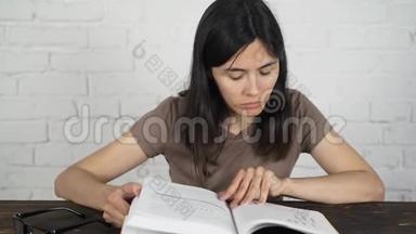 女孩坐在一张白色的桌子上，戴着眼镜看着一本书，日记。 视力不好。