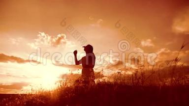 女孩在日落时双手交叉祈祷剪影生活方式。 女人跪着祈祷。 慢动作视频。 女孩