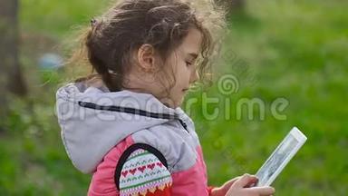 在森林里绿草如茵的背景下，春天带着平板电脑的女孩在玩网络游戏