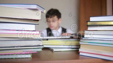 男孩坐在<strong>一</strong>张桌子旁，桌上放着<strong>一叠书</strong>。 孩子读<strong>书</strong>。 戴眼镜的男孩