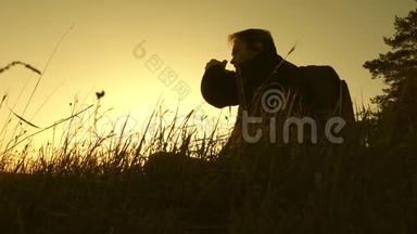 孤独的旅行者坐在山顶上，在热水瓶里喝咖啡。 游客喝热茶，看日落。 休息休息