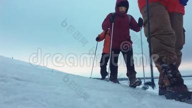 三个徒步旅行者带着徒步旅行杆，一个背包和雪鞋。 徒步旅行者小组冬季旅行愉快
