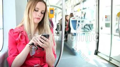 年轻的金发女人骑着电车，在手机、手机、手机上打字，拿着眼镜