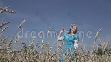在阳光明媚的日子里，年轻的女人穿着蓝色的裙子，在成熟的麦子里留着一头长长的长发，动作缓慢