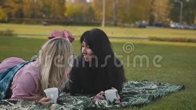 两个年轻的女人在城市公园玩得很开心。 日落时分，在一个温暖的公园野餐的女朋友