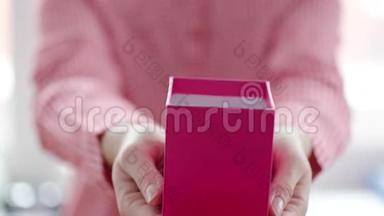 在女人手里用红丝带把粉色礼品盒收起来