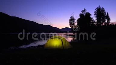 黄色帐篷在山湖畔花费.. 晚安。 在帐篷里，光线燃烧。