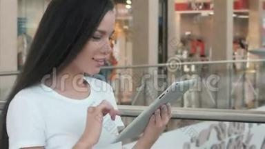 美丽的年轻女学生在购物中心使用她的白色平板电脑，快乐的大学生活