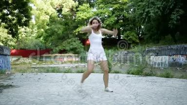 年轻的亚洲女人在城市公园外面跳现代舞蹈。 城市废墟和嘻哈涂鸦