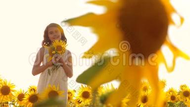 夏天，快乐的小女孩在田野上闻着一朵向日葵。 慢动作视频。 站在田野里的少女