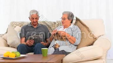 当她丈夫正在看报纸时，一位老妇人正在编织