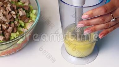 带有蔬菜和蛋黄酱的俄罗斯肉沙拉。 一个女人正在用搅拌机打蛋黄酱做沙拉。