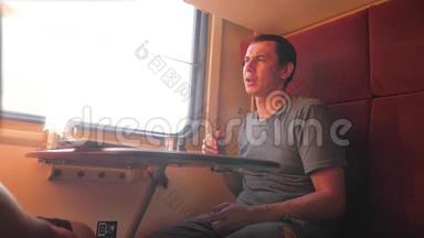 男人坐在<strong>火车车厢</strong>里，手里拿着铁路，喝着咖啡和茶。 慢动作生活方式视频。 两个人