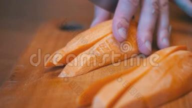 在家庭厨房的木制厨房板上用刀切割胡萝卜的女人手