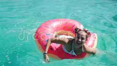阳光明媚的夏日，一位年轻貌美的女士戴着黑色比基尼的太阳镜，躺在充气的粉红色甜甜圈里漂浮在游泳池里