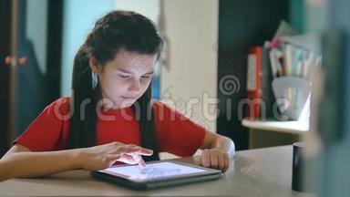 小女孩在玩数字平板电脑。 小女孩坐在桌边玩电子游戏中的数字生活方式平板电脑