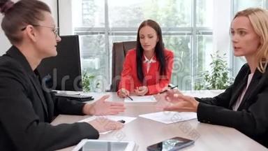 三个穿着商务套装的年轻漂亮女人坐在办公桌前讨论工作流程。 主管和下属