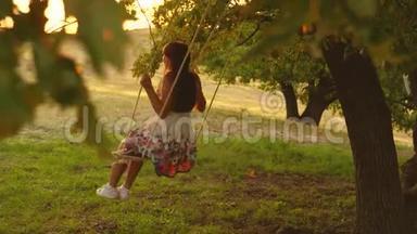 孩子们在公园的秋千上晒太阳。 年轻女孩在橡木树枝上的绳子上摆动。 少女喜欢飞行