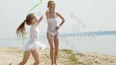 母亲和女儿穿着白色泳衣，在沙滩上用体操丝带跳舞。 夏天，黎明
