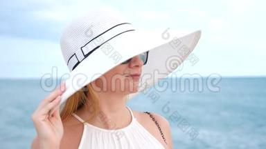 一位身穿白色宽边帽子和<strong>太阳镜</strong>的优雅<strong>女士</strong>欣赏海景。 4k，慢镜头