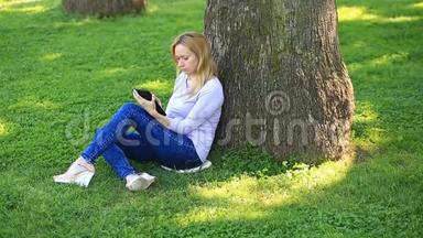 英俊的女人坐在棕榈树下，用智能手机上网