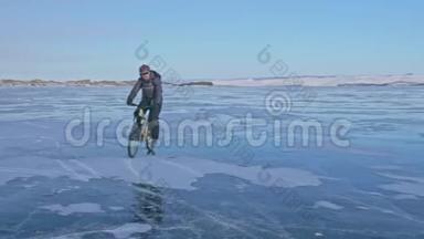 人在冰上骑自行车。 骑自行车的人穿着灰色的羽绒服，背包和头盔。 冰冻的冰