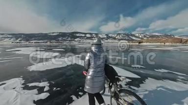 女人在冰上骑着自行车走着。 女孩穿着银色的<strong>羽绒服</strong>，背包和头盔。 冰冰