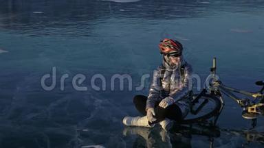 女人在冰上骑自行车。 女孩穿着银色羽绒服，自行车背包和头盔。 这就是