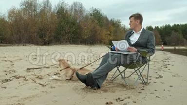 成熟的商人，狗坐在河边放松。 穿西装用笔记本电脑的人。