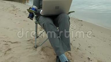 成熟的商人坐在河边放松。 穿西装用笔记本电脑的人。