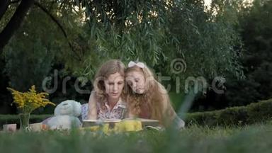 一对幸福的母女在相册里看照片读一本书。 一家人在城市公园野餐，在温暖的晚上。