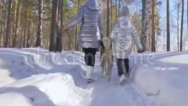 美丽的女人和小孩在冬天的森林里和哈士奇的狗散步。 快乐的年轻母亲和女儿