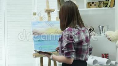 一位年轻女子站在画架后面的一张画布上，在一个大气车间里画一幅画