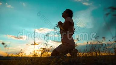 女孩在日落时双手交叉祈祷剪影。 慢动作视频。 女孩双手交叉祈祷祈求上帝