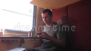 男人坐在<strong>火车车厢</strong>里，拿着智能手机，喝着咖啡和茶。 慢动作视频。 男人