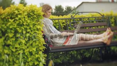 有笔记本电<strong>脑</strong>的女人在一个美丽的绿色公园的长凳上放松。 一个常年在树<strong>洞</strong>里工作的年轻女人