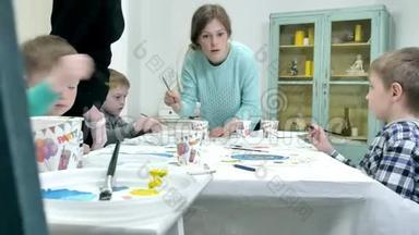 <strong>孩子</strong>们在教室里围着桌子坐在一起<strong>画画</strong>。 和他们在一起的是他们年轻美丽的老师