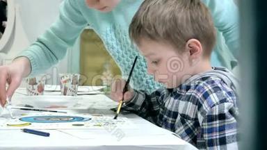 孩子们在教室里围着桌子坐在一起画画。 和他们在一起的是他们年轻美丽的老师