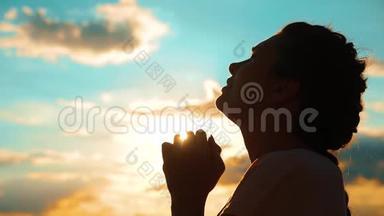 女孩在祈祷。 女孩在日落时交叉双手祈祷剪影。 慢动作视频。 女孩的生活方式让她双手合拢