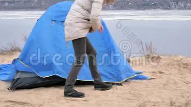 迷人的年轻旅游妇女戴着红帽子，在海岸森林附近收集一个旅游帐篷