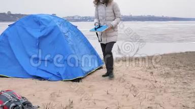 迷人的年轻旅游妇女戴着红帽子，在海岸森林附近收集一个旅游帐篷
