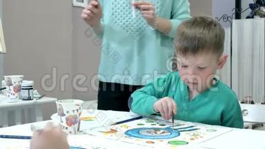 孩子们在教室里围着桌子坐在一起画画。 和他们在一起的是他们年轻美丽的老师