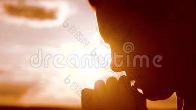 女孩祈祷。 女孩在日落时双手交叉祈祷剪影。 慢动作视频。 女孩的生活方式让她双手合拢